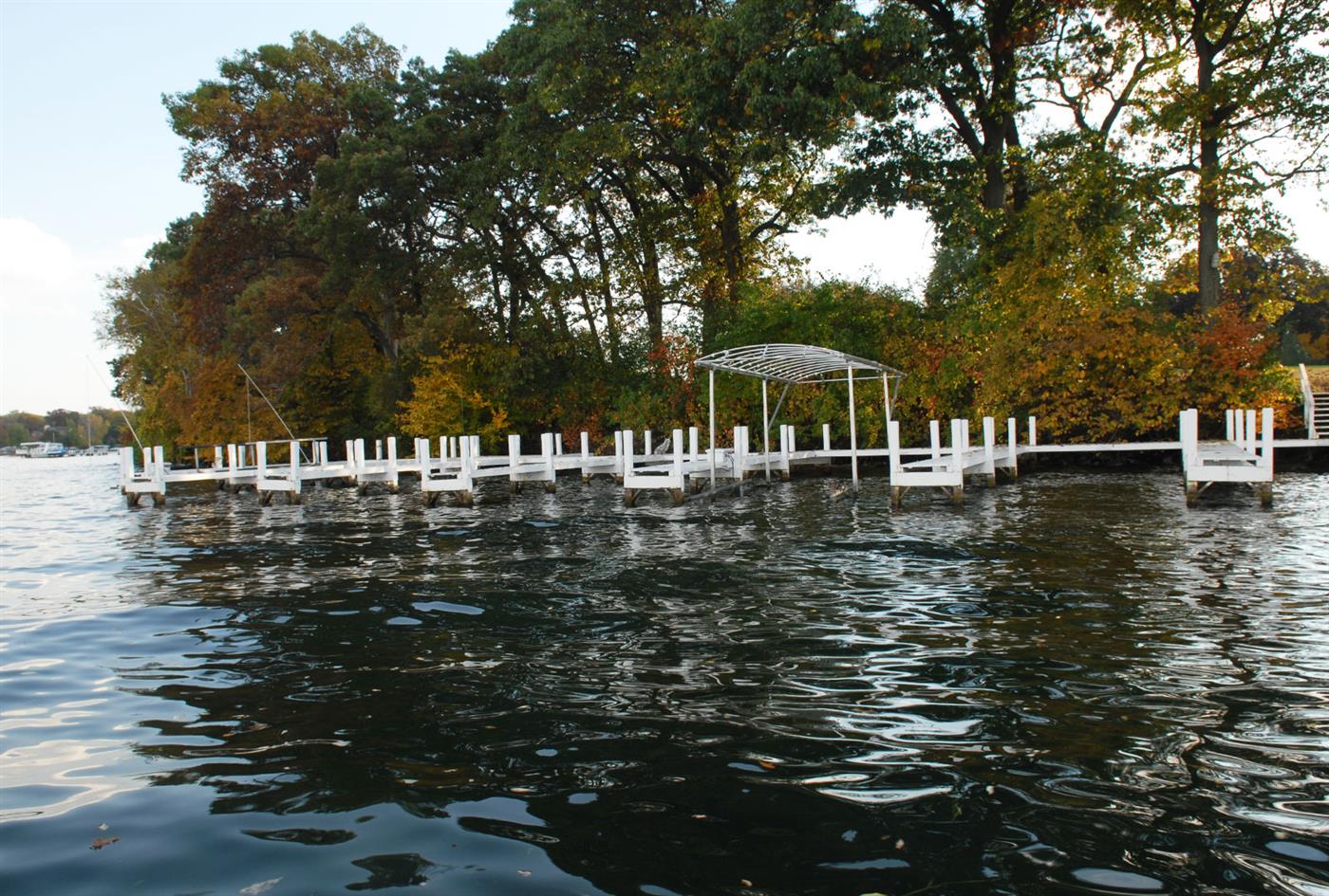 Long finished white pier with canopy frame along a wooded Geneva Lake shoreline