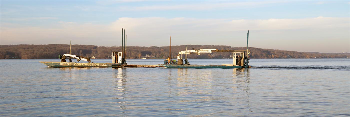 Reed's barges with cranes crossing calm water in golden light